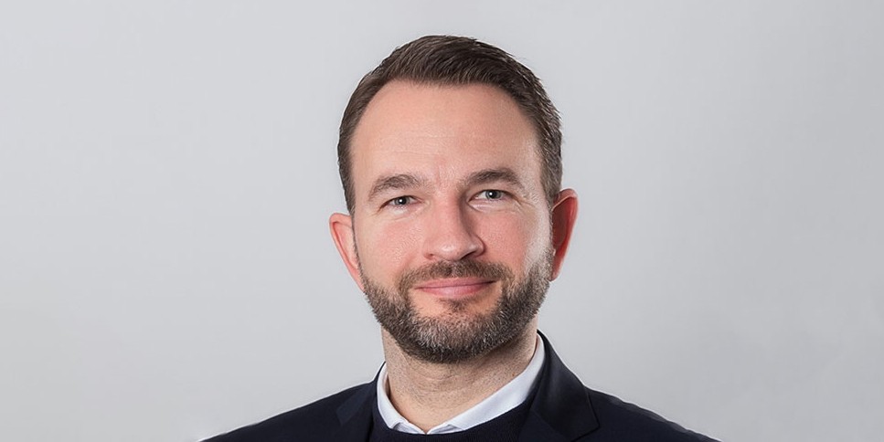 Porträt des OEV-Mitarbeiters Daniel Spiecker im Anzug, der freundlich in die Kamera blickt