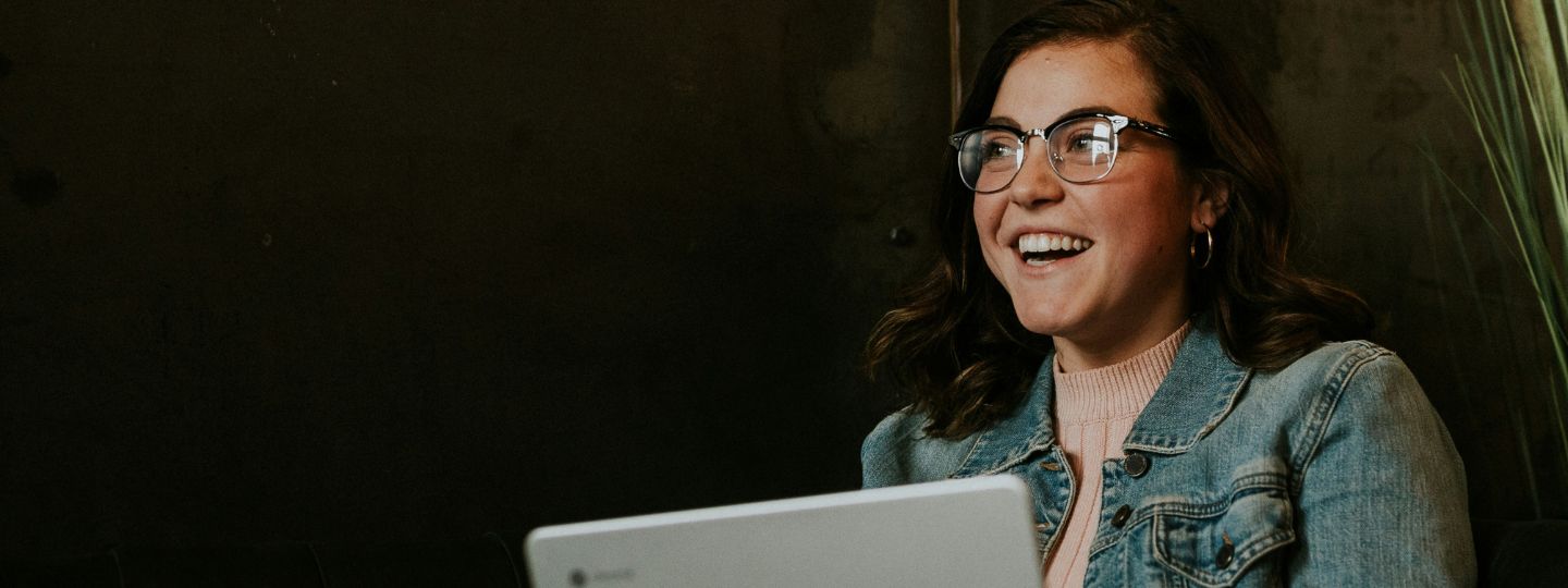 Frau sitzt auf einem braunen Holzstuhl, während sie einen silbernen Laptop im Zimmer benutzt und sich in das Kundenportal einloggt