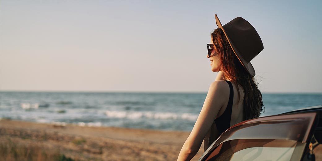 Frau steht entspannt am Auto am Strand