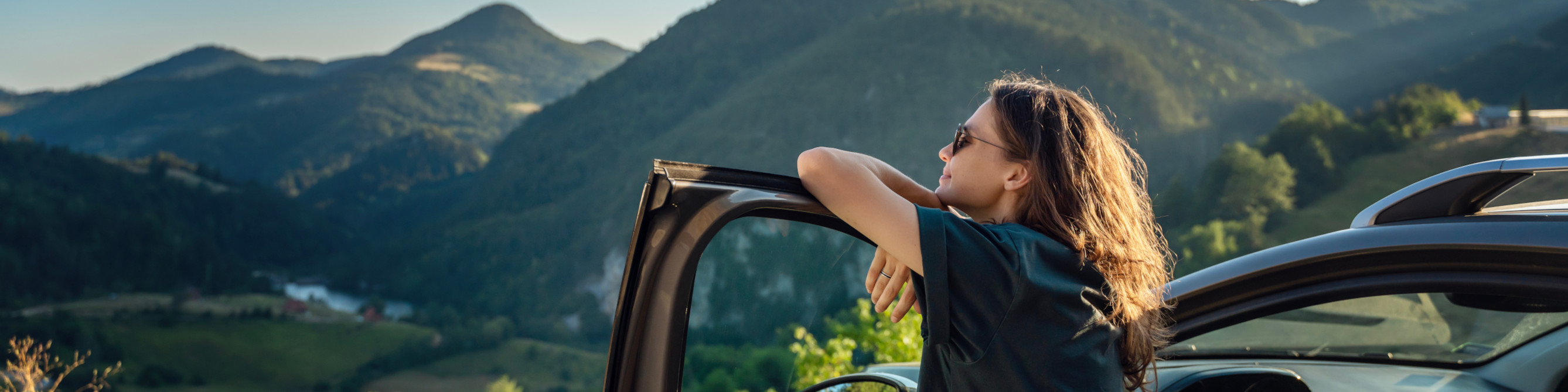 Junge Frau steht am Auto und schaut auf die Berge